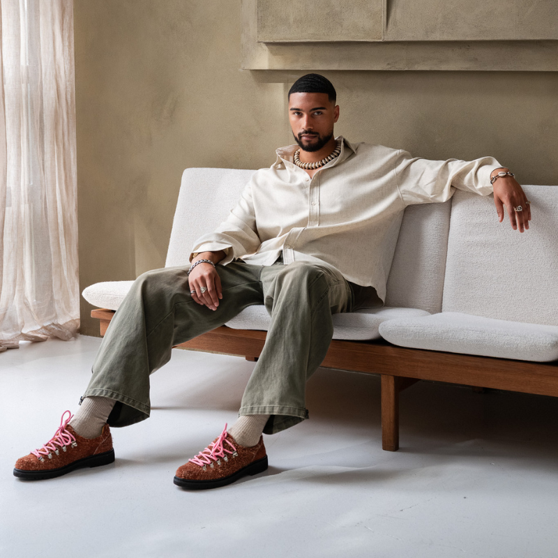Man seated on a sofa wearing red Paper Straight derbies from A/W 25 Drop One