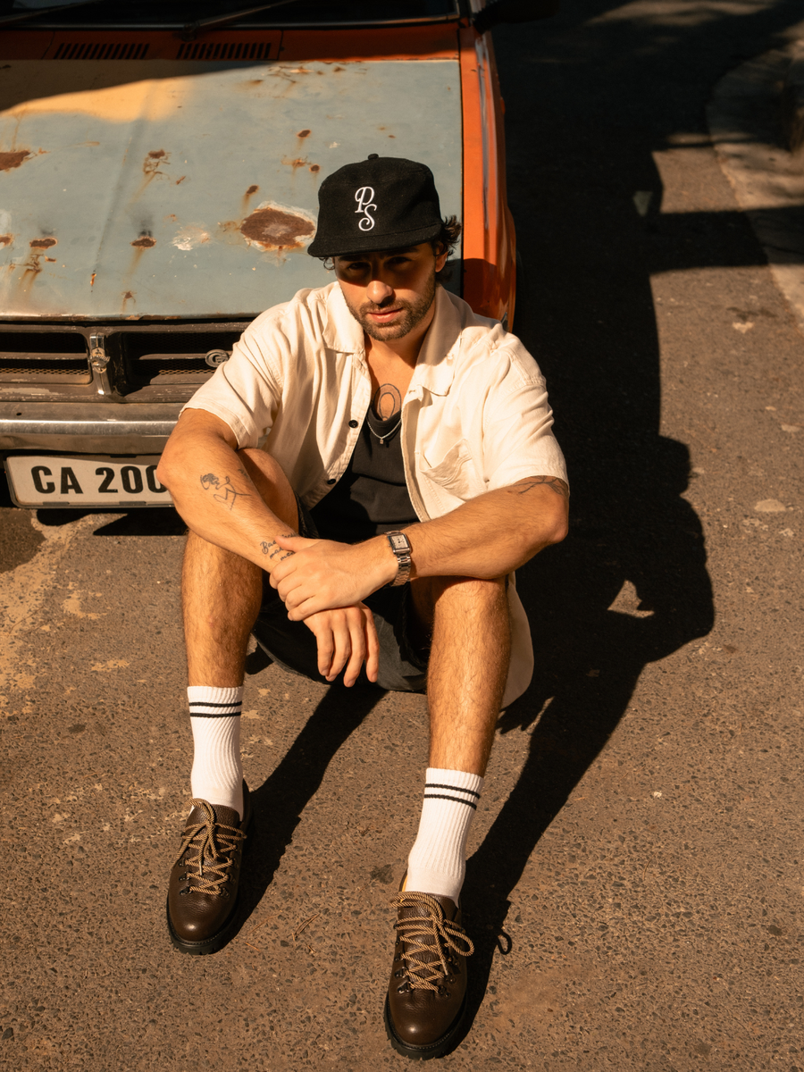 Man in a Paper Straight cap and derbies seated in front of a vintage car in Cape Town