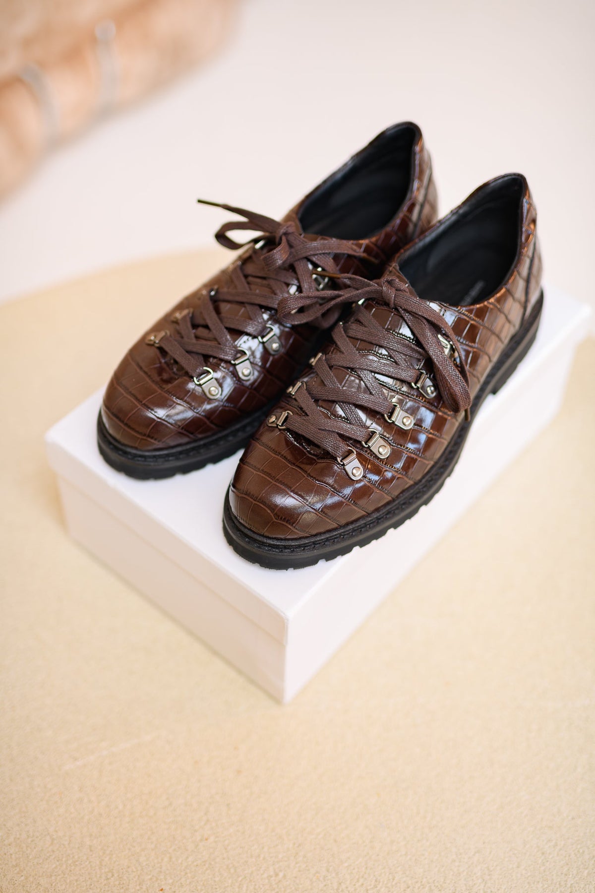A pair of brown croc-textured derbys on a white shoebox.