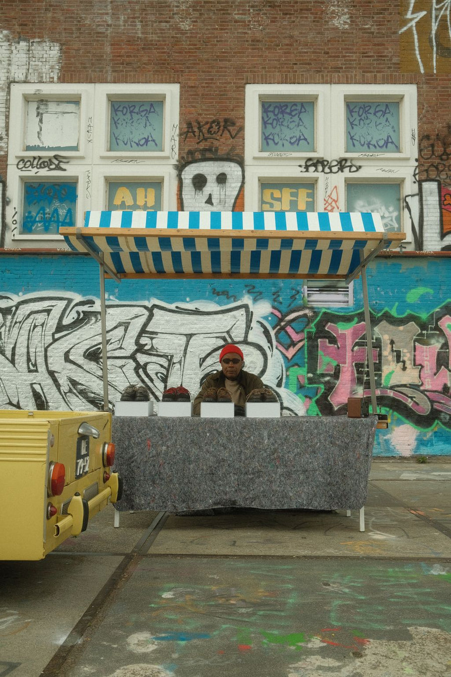 Market stall in front of a graffiti covered building in Amsterdam next to a yellow vintage car