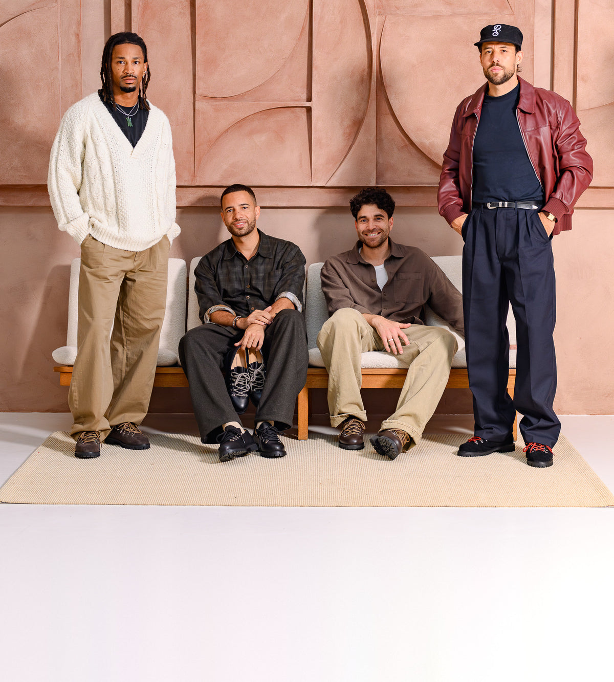 Four men in Paper Straight Autumn Winter 26 footwear, two standing and two seated on a bench against a terracotta wall