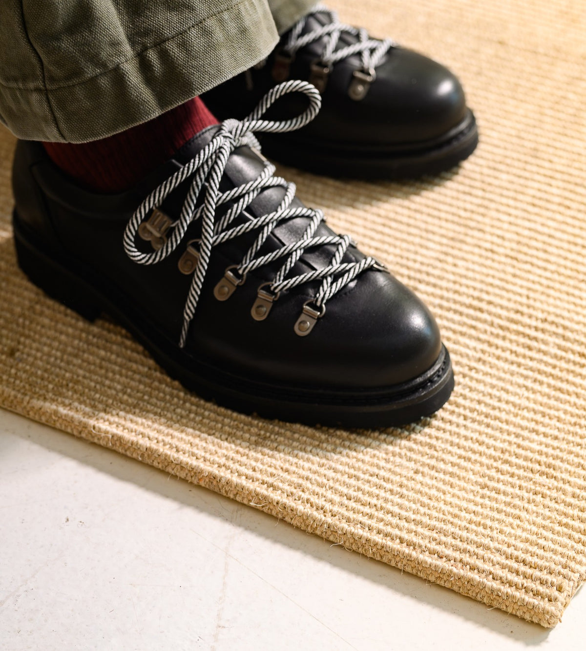 Paper Straight Summit Derby Signature in black full-grain leather with white rope laces, worn on a woven rug