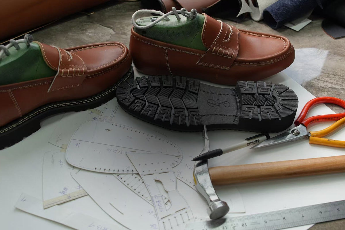 Two Paper Straight derbies on a workbench beside a moulded rubber outsole hand-drawn patterns and shoemaking tools