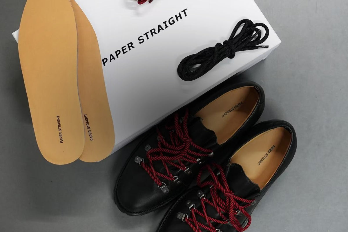 Paper Straight Heritage Derby in black cowhide leather with red rope laces beside its box leather insoles and spare laces